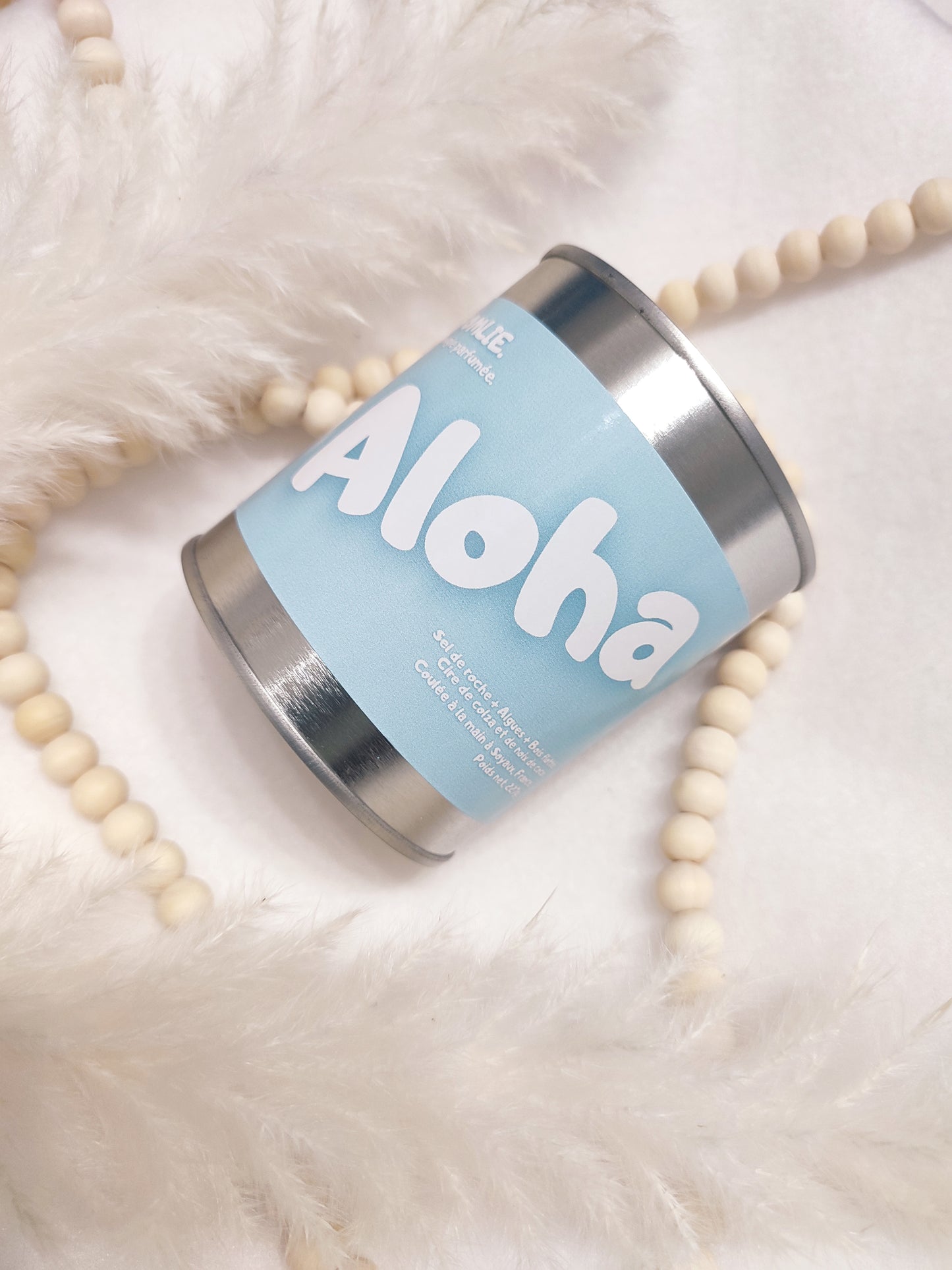 Bougie parfumée "Aloha" bleue avec à ces cotés des bijoux et des plumes.