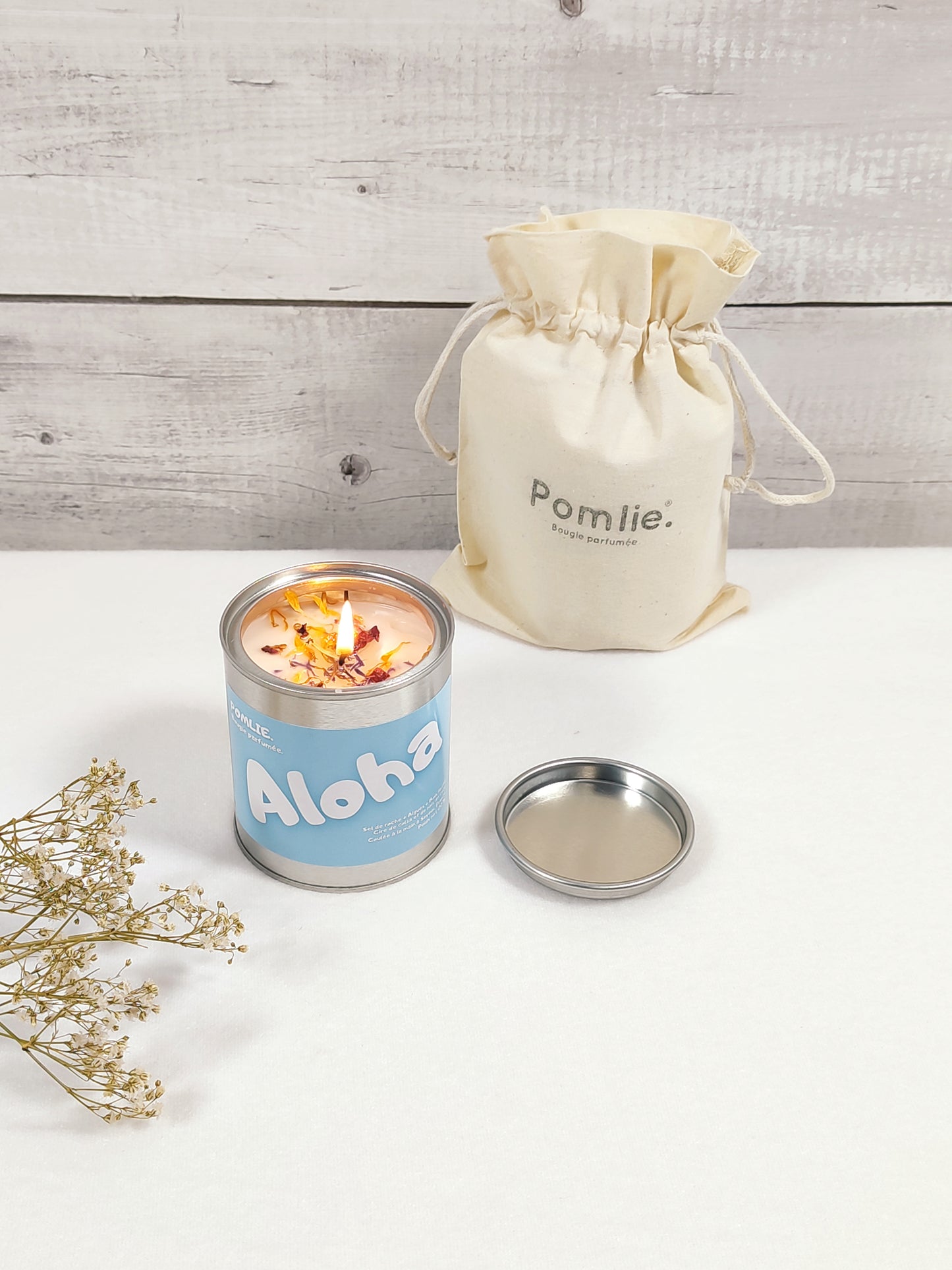 Bougie Pomlie en métal bleue avec l’inscription ‘Aloha’ avec à coté d'elle sont sac en coton.