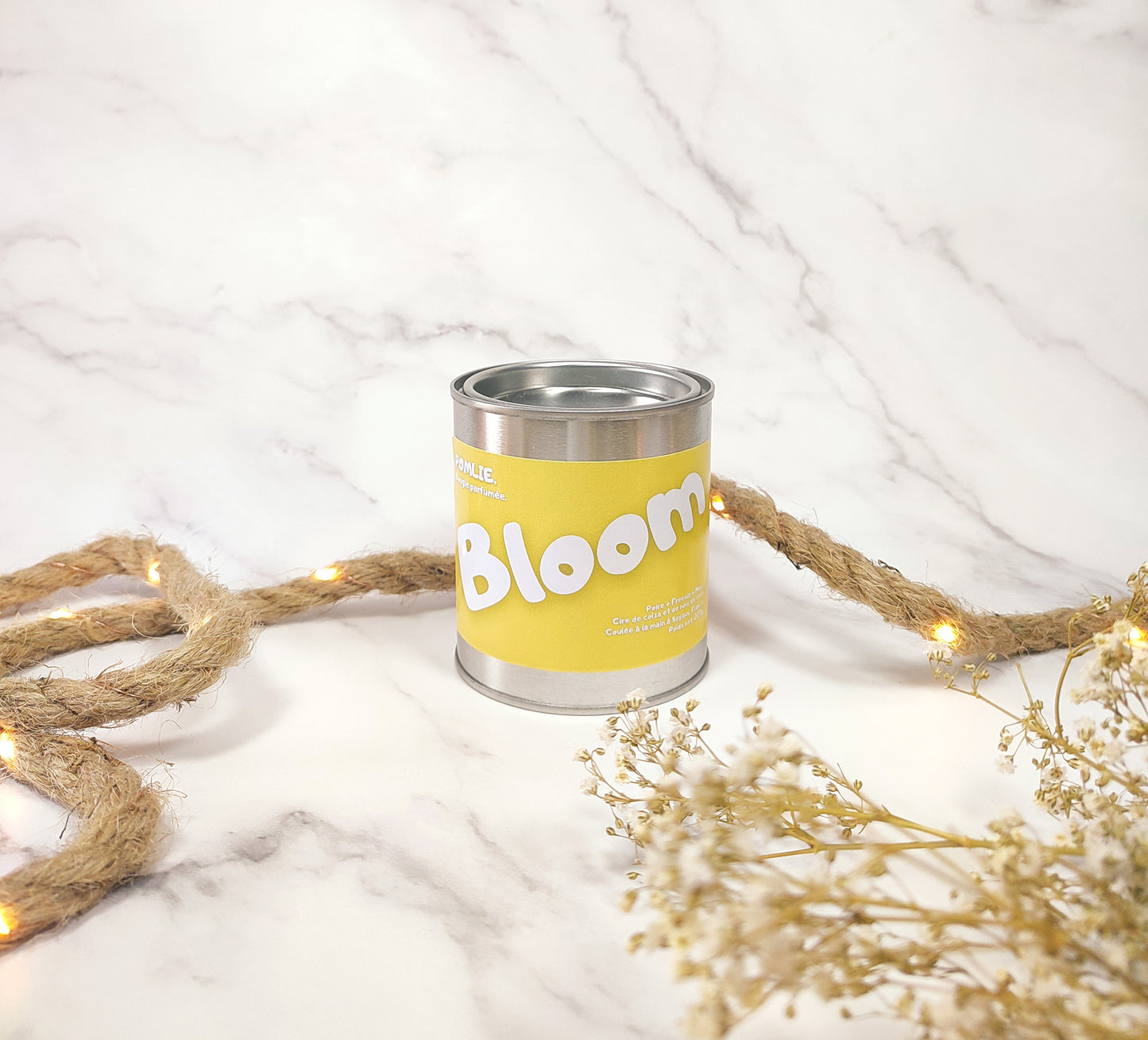 Bougie parfumée Bloom allumée avec corde de décoration et fleurs séchées.