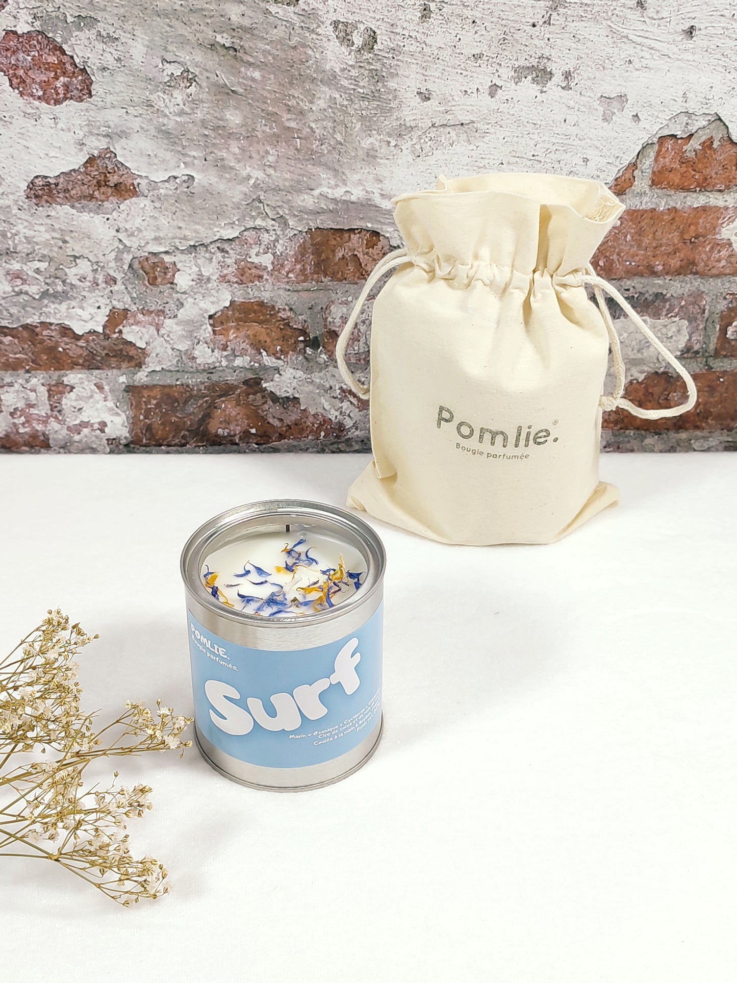 Bougie Pomlie Surf dans une boîte en métal bleu avec sac en coton.
