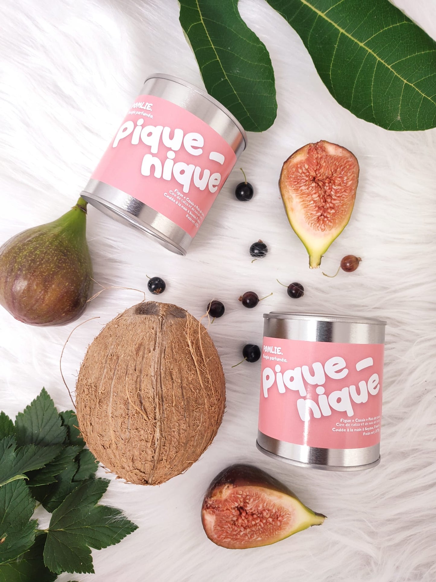 Bougie Pomlie Pique-nique dans une boîte en métal rose avec figues, cassis et noix de coco à ces côtés.