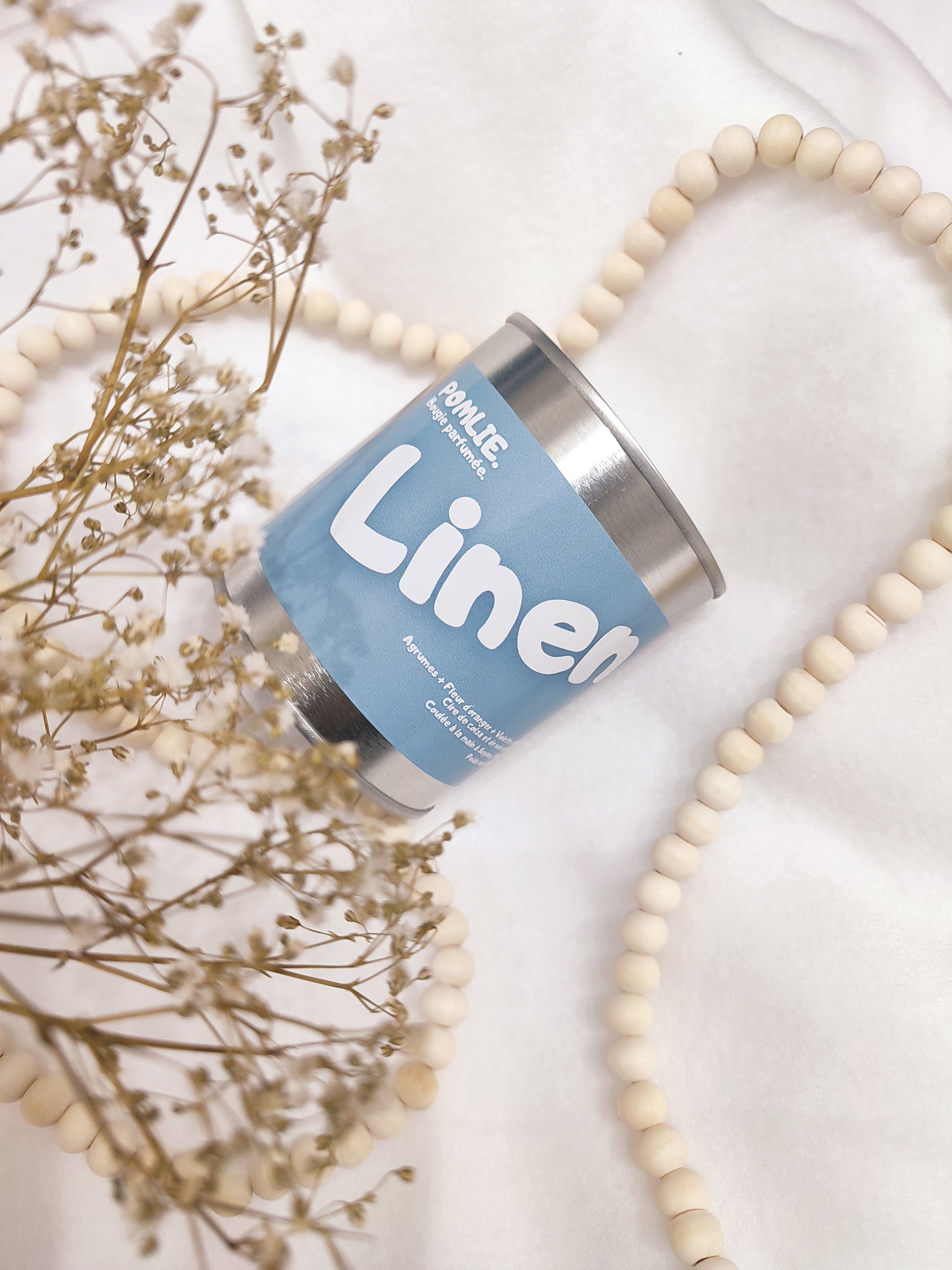 Bougie parfumée Linen bleue avec bijoux et fleurs séchées.