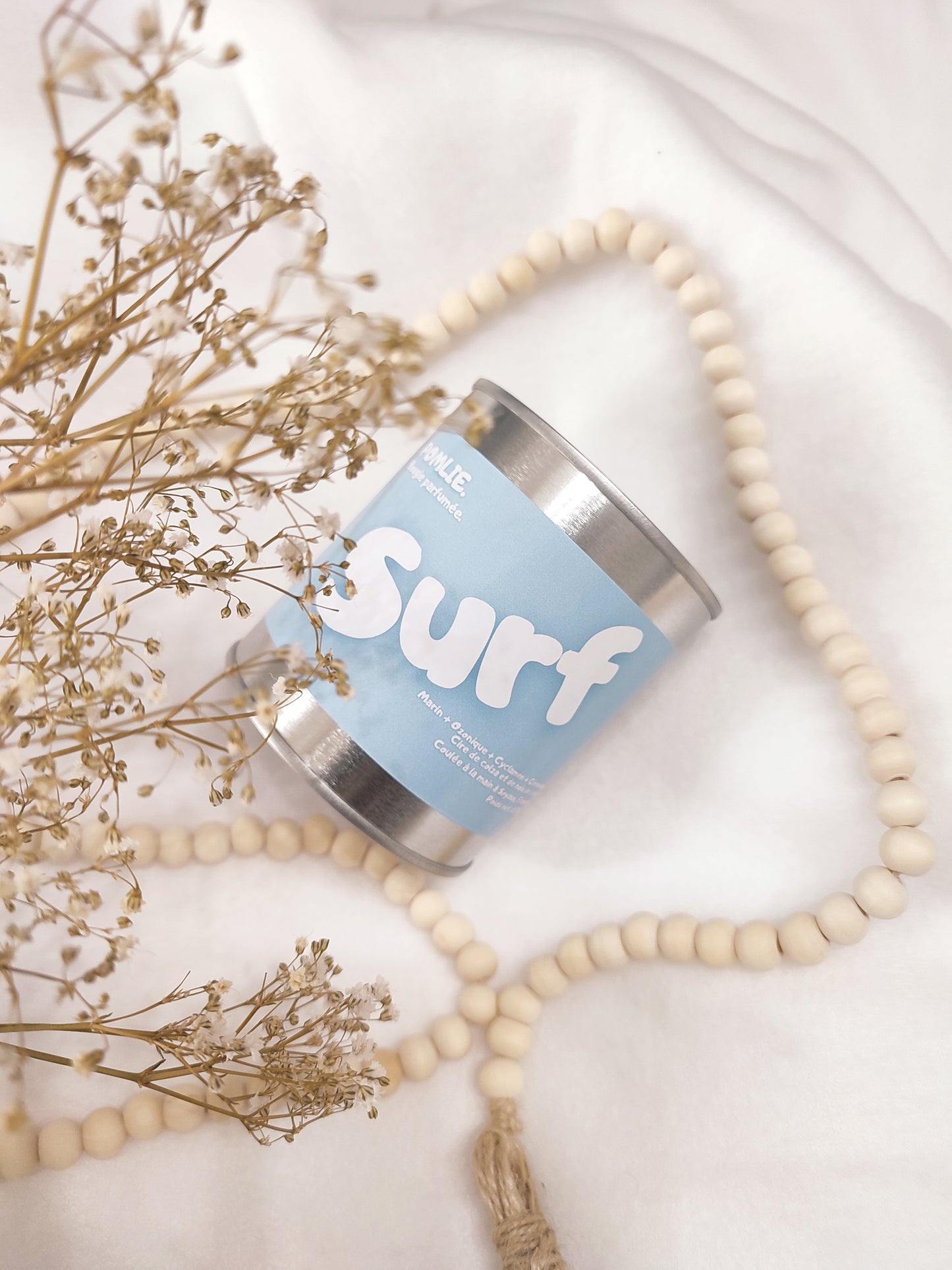 Bougie parfumée Surf bleue avec bijoux et fleurs séchées.